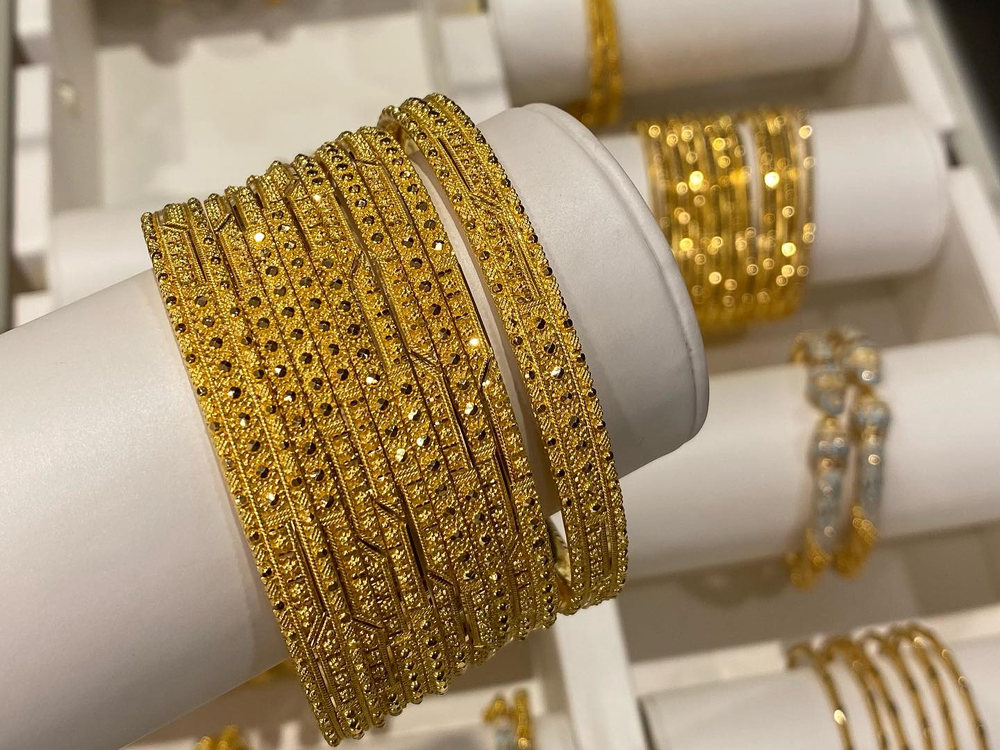 A woman's wrist stacked with patterned 22 carat gold bangles