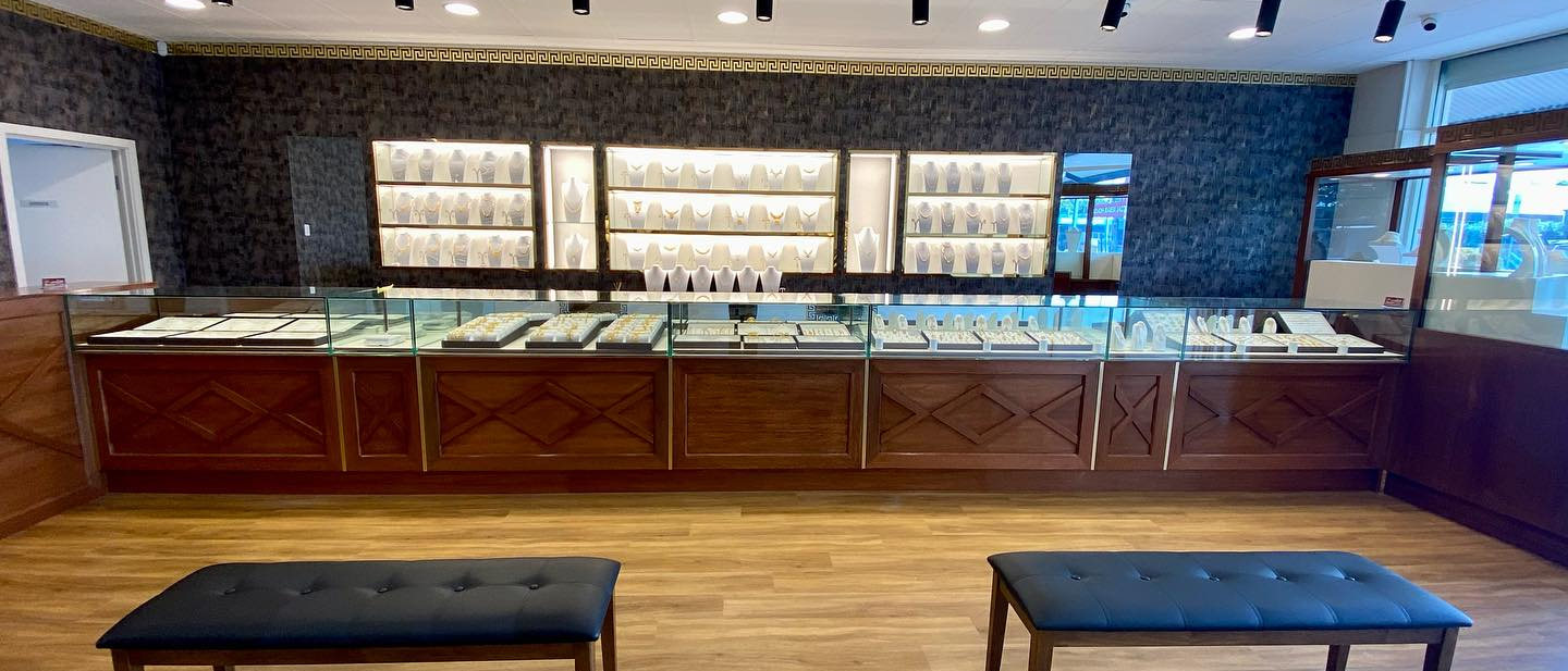 The shop floor at Aroos Jewellers: the full run of glass counters, the lit wall cases of gold sets behind them, and two benches on the timber floor
