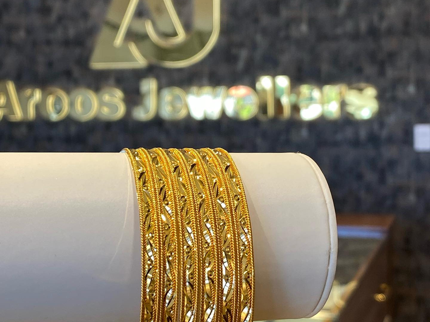 Gold bangles being slid onto a customer's wrist across a lit shop counter