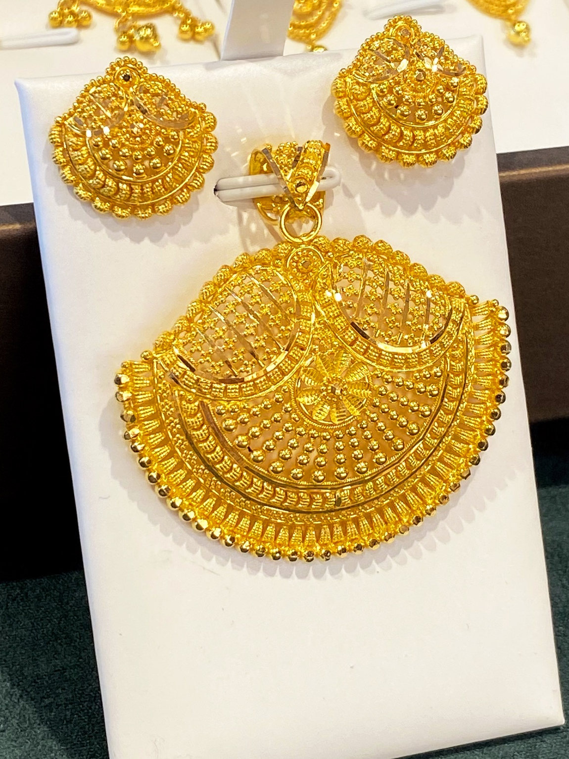 A 21 carat gold fan pendant and its matching earrings on a white card in the cabinet at Aroos Jewellers, the filigree and granulation close enough to count
