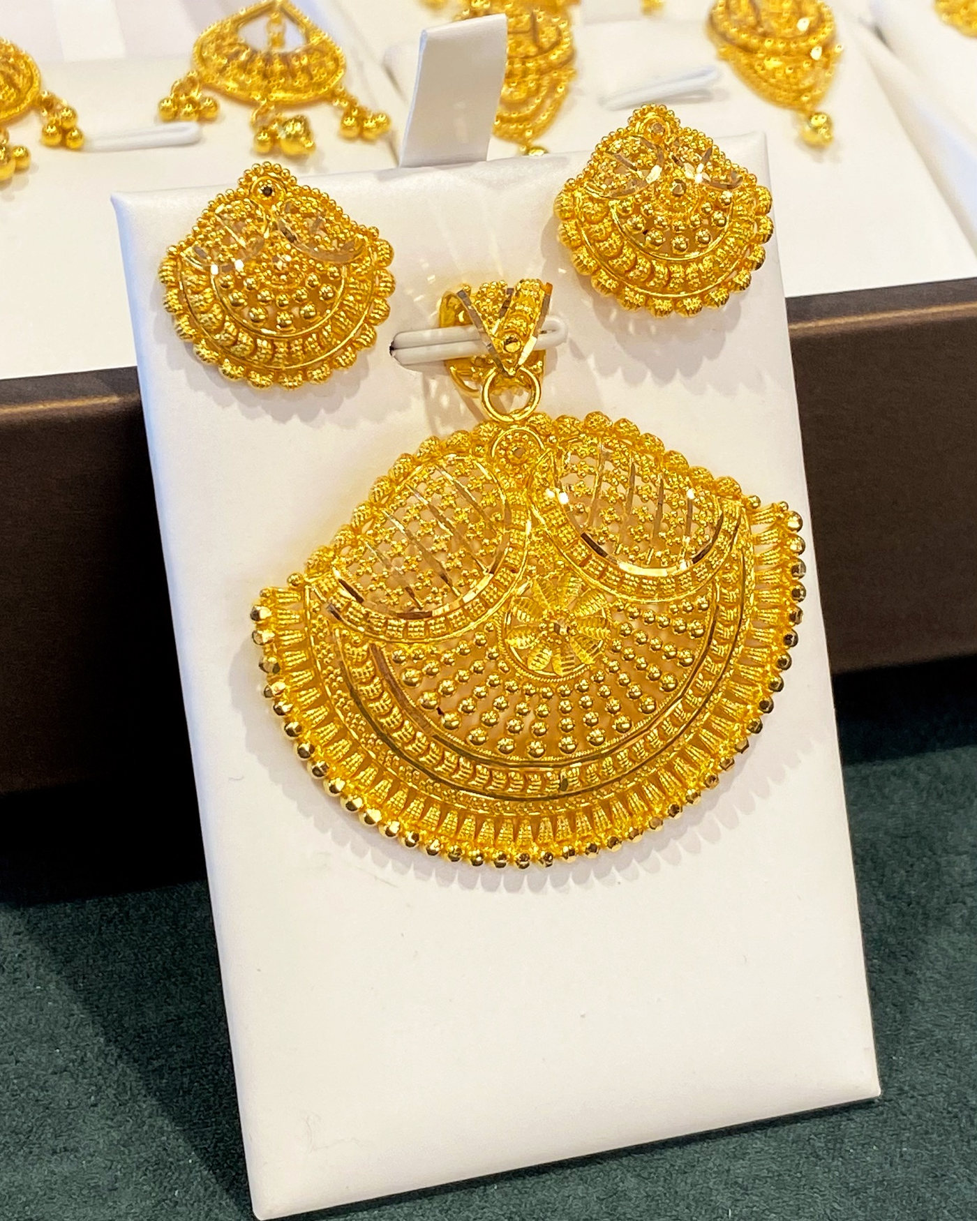 A 21 carat gold pendant and its matching earrings on a white card, the fan-shaped pendant worked in fine filigree
