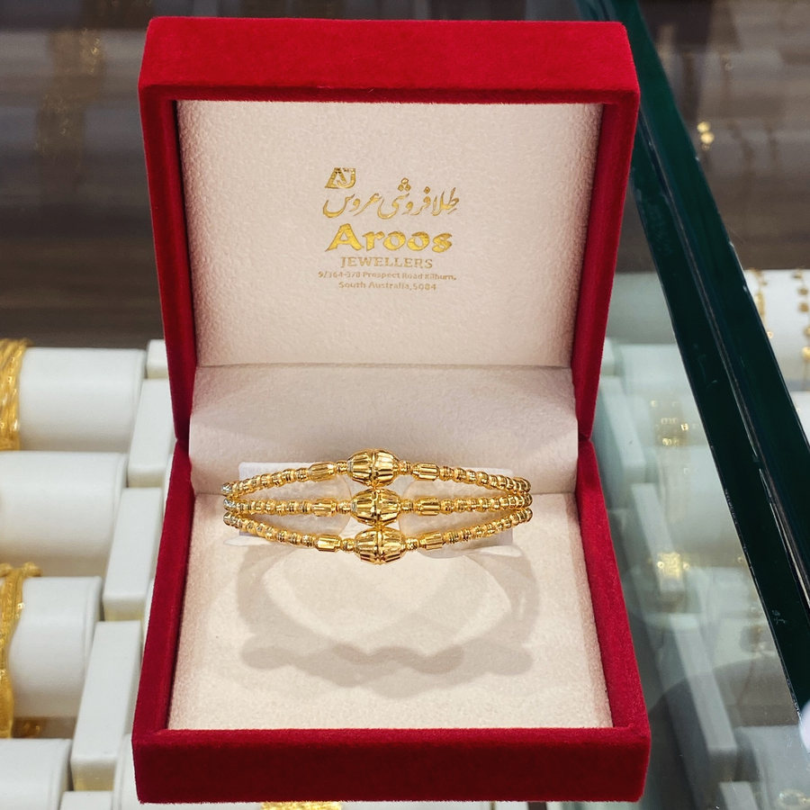 A 21 carat gold bangle in the shop's own maroon presentation box, the Aroos Jewellers name and address printed inside the lid
