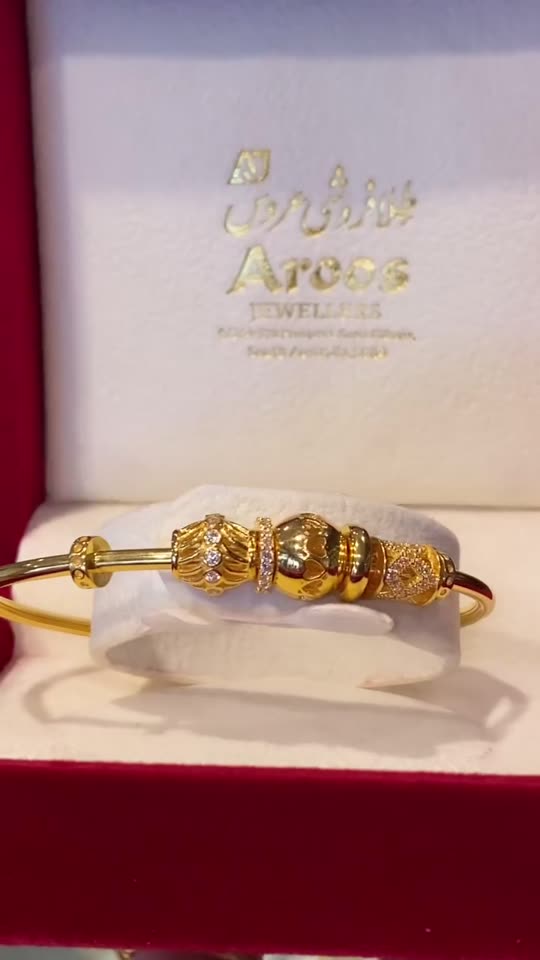 A 21 carat gold bangle in the shop's own maroon box, the name Aroos Jewellers printed in gold inside the lid