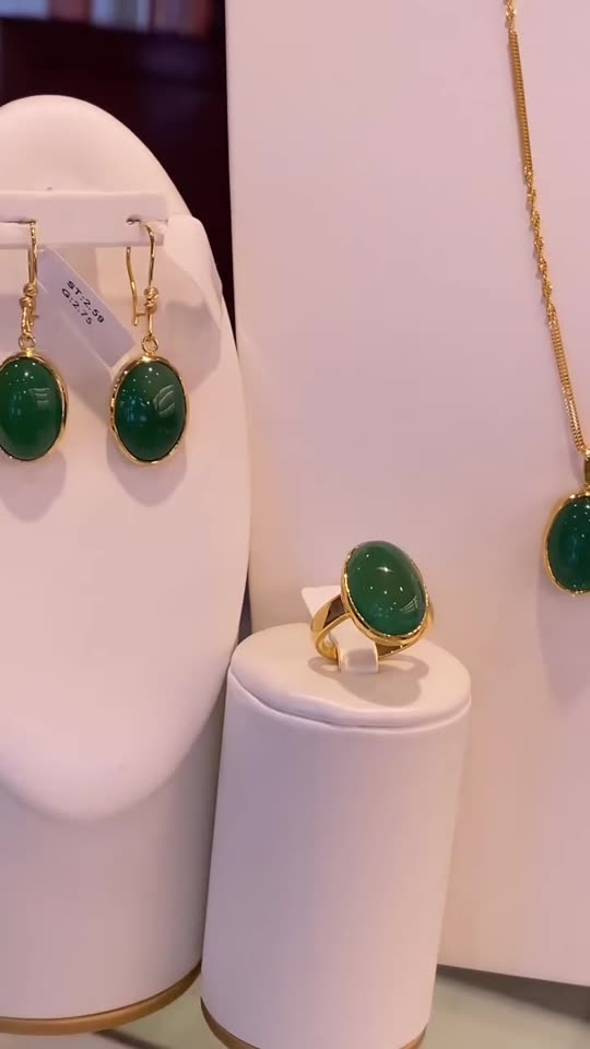 Green stone drop earrings, pendant and ring in 21 carat gold, set out together on white stands
